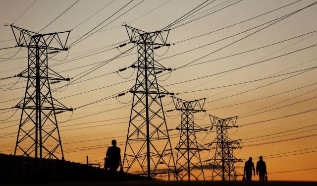 FILE PHOTO: Locals walk past electricity pylons during frequent power outages from South African utility Eskom, caused by its aging coal-fired plants, in Soweto, South Africa, July 3, 2022. REUTERS/Siphiwe Sibeko/File Photo