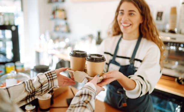 Smiling barista- girl giving take away coffee cups to a customers.