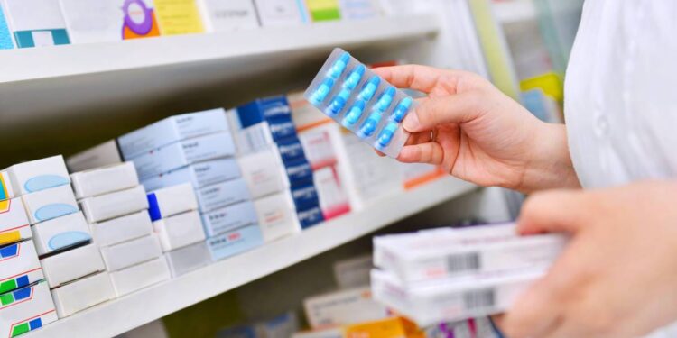 Pharmacist holding medicine box and capsule pack in pharmacy drugstore.